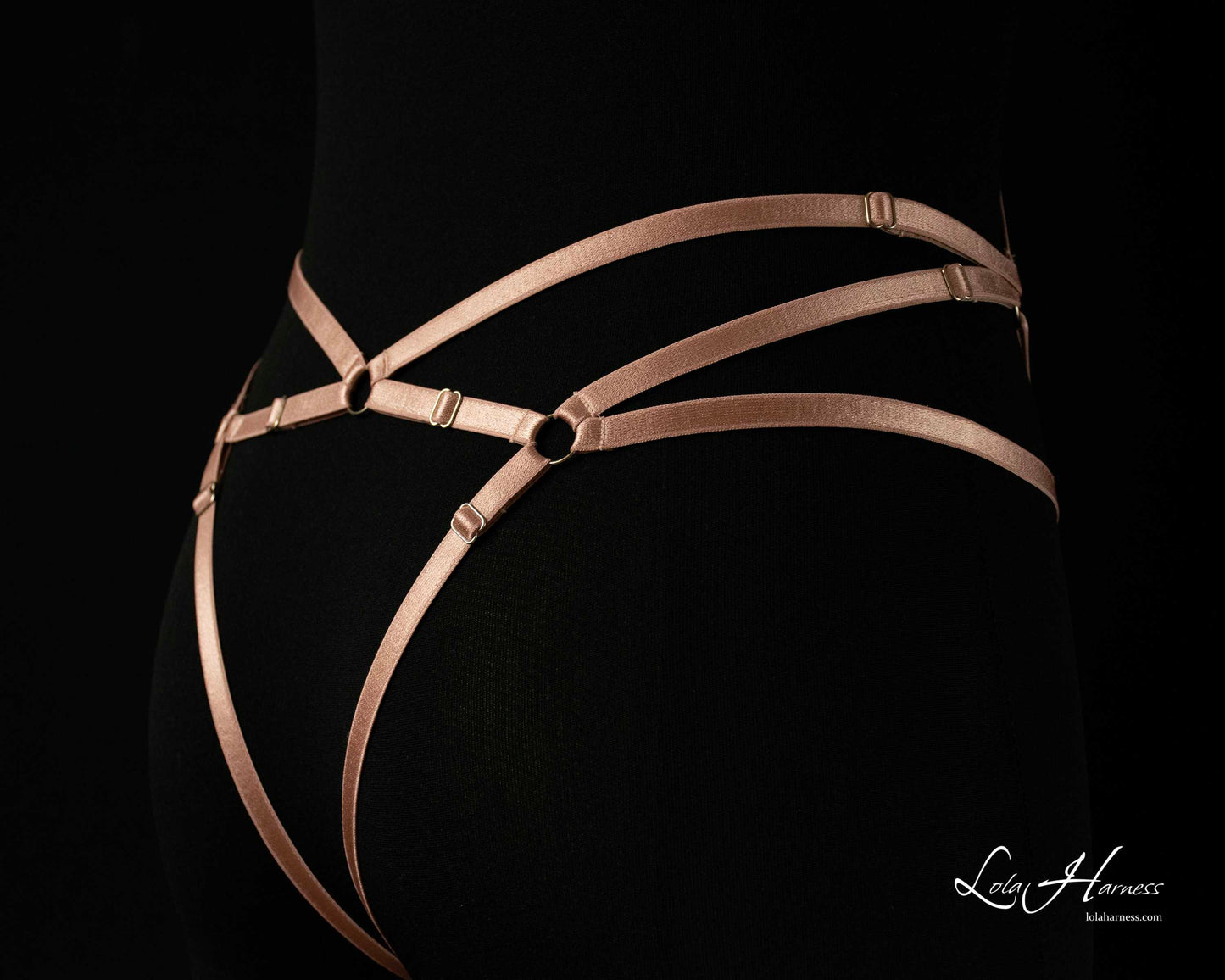 Side close-up of the back bottom of The Carry harness playsuit on a mannequin in dusty rose, emphasizing the strap placement.