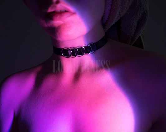 Front view of The Claire harness choker on a model in black, featuring a wide adjustable elastic band with five rings.