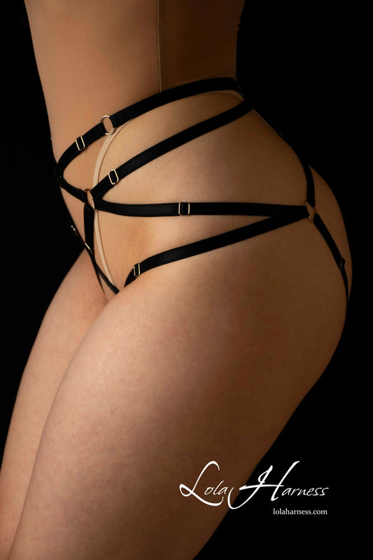 Another front view of The Elsa black adjustable strappy harness bottoms on model, highlighting the flattering fit and adjustable straps over a beige mesh bodysuit